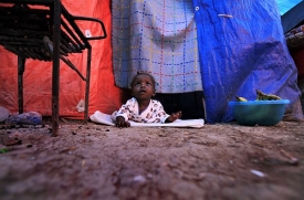 Desetiměsíční dítě u provizorního přístřešku v táboře pro uprchlíky.
